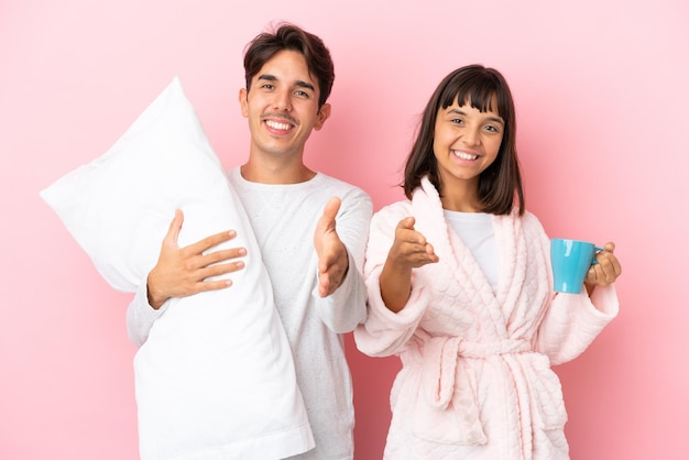 Young couple in pajamas isolated on pink background shaking hands for closing a good deal