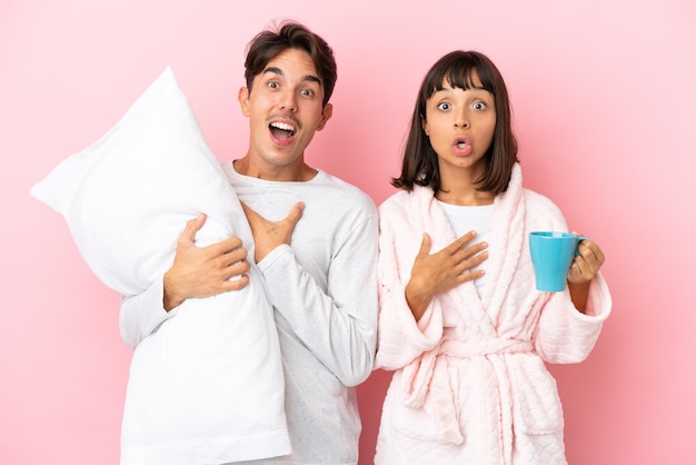 Young couple in pajamas isolated on pink background surprised and shocked while looking right