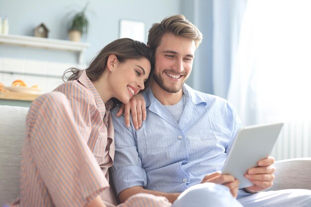 Young couple in pajamas watching media content online in a tablet sitting on a sofa in the living room.