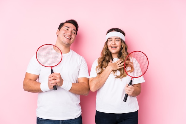 Young couple playing badminton isolated laughs out loudly keeping hand on chest.