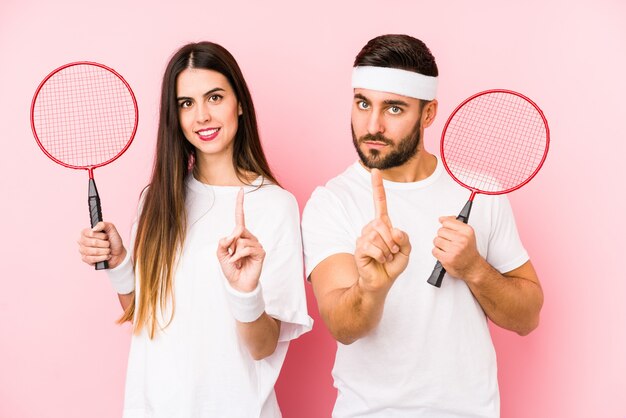 Young couple playing badminton isolated showing number one with finger