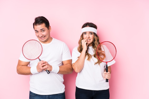 Young couple playing badmintover isolated biting fingernails, nervous and very anxious.