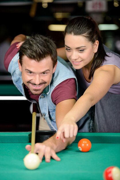 Young couple plays billiards in the dark billiard club