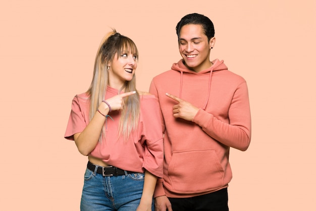 Young couple pointing to the side to present a product over pink background