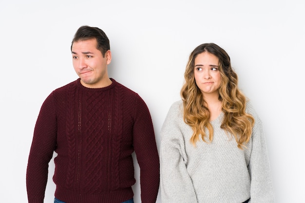 Young couple posing in a white wall confused, feels doubtful and unsure.