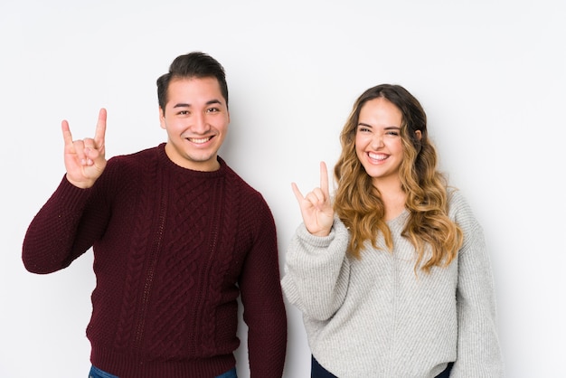 Photo young couple posing in a white wall showing a horns gesture as a revolution concept.