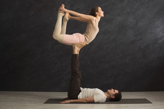 함께 체육관에서 매트에 acroyoga를 연습 하는 젊은 부부. 남자 다리에 균형을 잡는 여자. 파트너 요가, 유연성, 신뢰 개념, 복사 공간