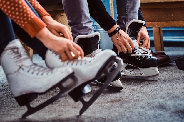 Photo young couple preparing to a skating. close-up photo of their hands tying shoelaces of ice hockey skates in a locker room