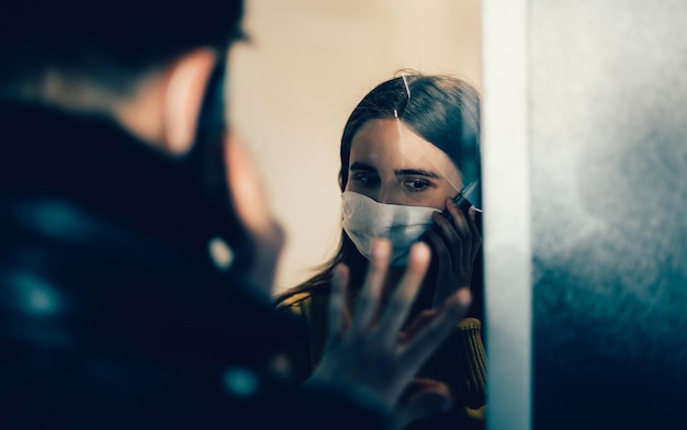 Young couple in protective masks communicating with each other through the glass