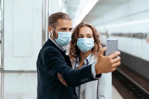 Foto giovani coppie in maschere protettive che si fanno selfie in metropolitana