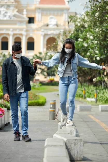 Young couple in protective masks walking in city park and enjoying romantic date