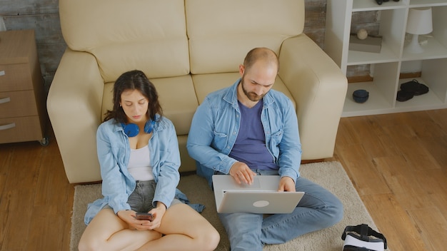 Young couple relaxing on carpet using laptop and smartphone