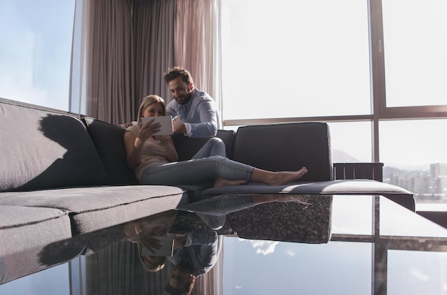 Photo young couple relaxing at home using tablet computer reading in the living room near the window on the sofa couch.