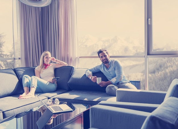 Young couple relaxing at  home using tablet computer reading in the living room near the window on the sofa couch.