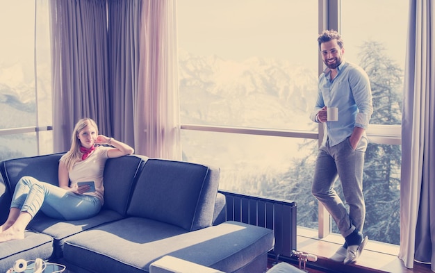 Young couple relaxing at  home using tablet computer reading in the living room near the window on the sofa couch.