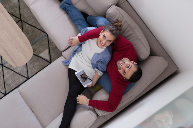 Young couple relaxing at  home using tablet computers reading in the living room on the sofa couch.