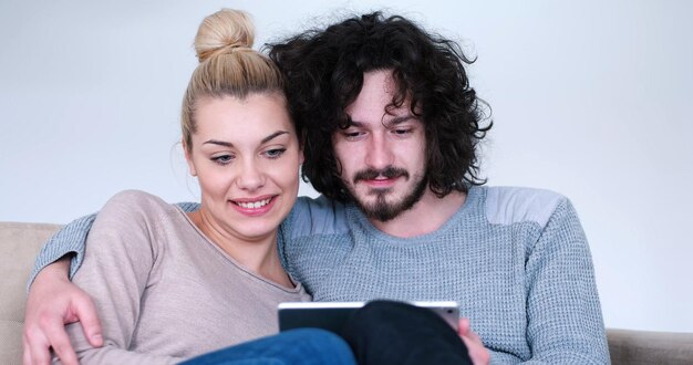 Photo young couple relaxing at luxurious home with tablet computers reading in the living room on the sofa couch.