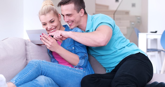 Young couple relaxing at luxurious home with tablet computers reading in the living room on the sofa couch.