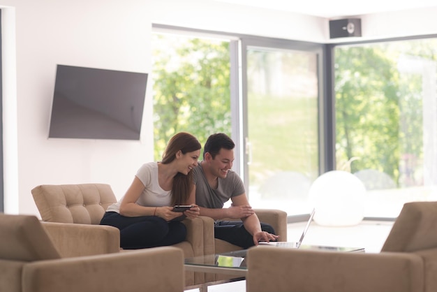 Young couple relaxing at luxurious home with tablet and laptop computers reading in the living room on the sofa couch.