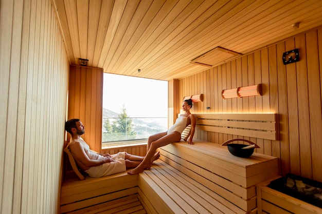 Young couple relaxing in the sauna and watching winter forest through the window