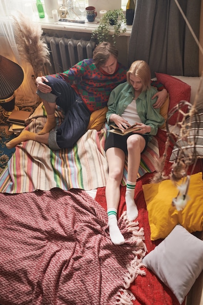 Young couple relaxing together on the bed and reading a book together in the room at home