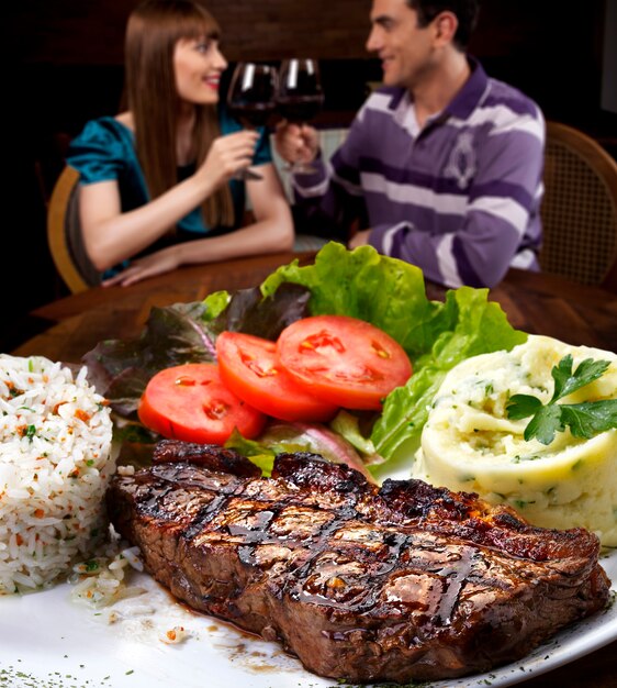 Foto giovani coppie al ristorante che mangiano carne di bistecca.