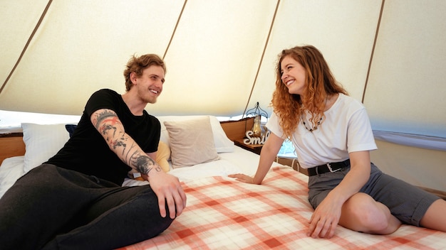 グランピングでテントのベッドで休んでいる若いカップル笑顔と笑い