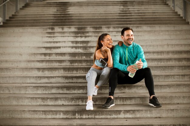 Young couple resting during training with bottle of water in urban environment