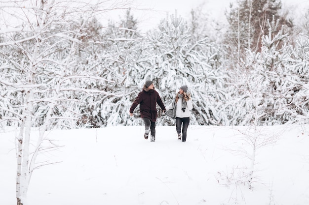 Young couple running on a snowy winter field near pine