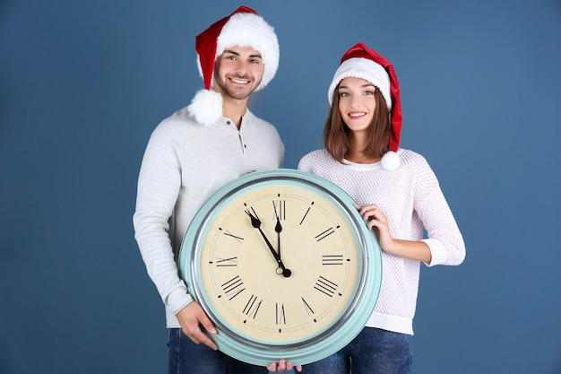 Young couple in Santa hats with clock on color space. Christmas countdown concept