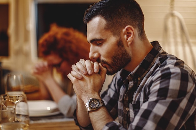 Young couple saying grace while having dinner at dining table Focus is on man