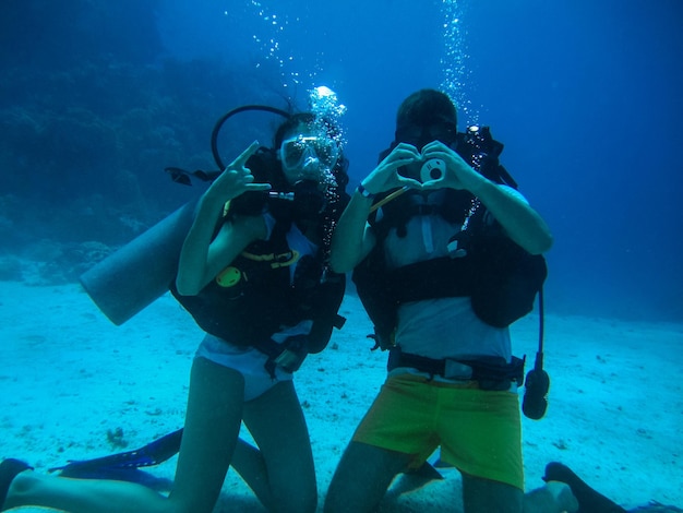 Young couple on the seafloor looking at the camera and show different gestures while diving