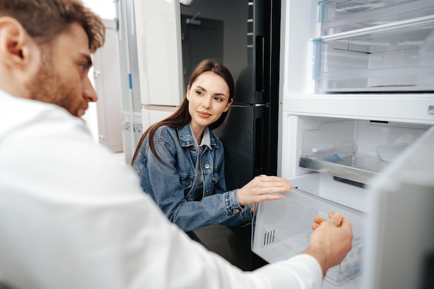 Young couple selecting new refrigerator in household appliance store