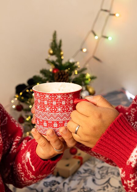 Photo young couple sharing at christmas a red cup with christmas decorations that has hot chocolate