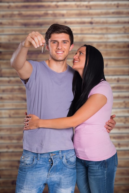 Young couple showing keys to house against wooden planks