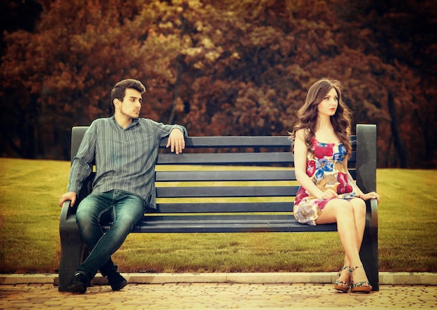 Young couple sitting apart on the bench in the park