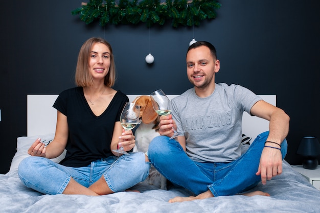 Young couple sitting on a bed in the bedroom, hugging. Near them is their dog. Domestic animal Beagle