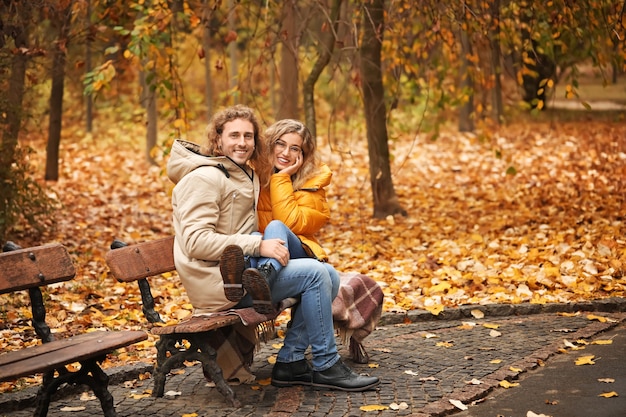 Giovani coppie che si siedono sulla panchina nel parco d'autunno