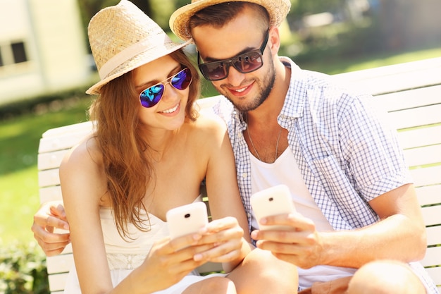 a young couple sitting on a bench with smartphones