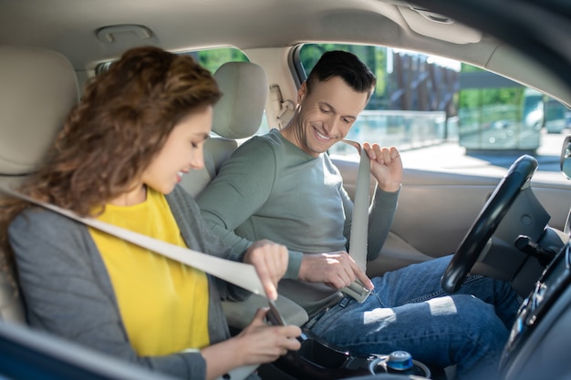 Young couple sitting in the car, woman fixing her safety belt