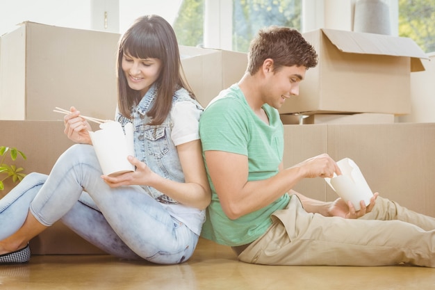 Young couple sitting on the floor and eating noodle in their new house