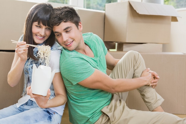 Young couple sitting on the floor and eating noodle in their new house