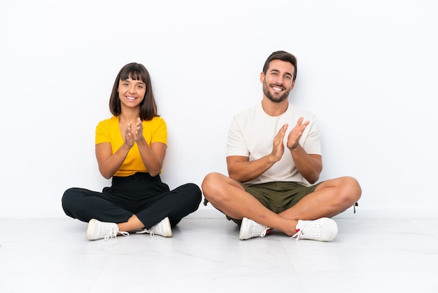 Photo young couple sitting on the floor isolated on white background applauding after presentation in a conference