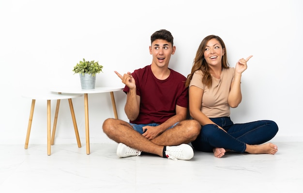 Photo young couple sitting on the floor on white intending to realizes the solution while lifting a finger up