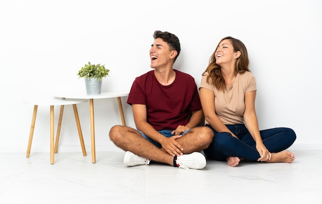 Young couple sitting on the floor on white laughing in lateral position
