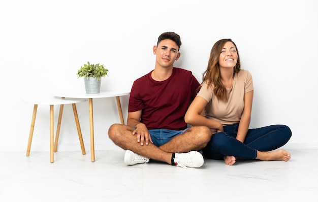 Young couple sitting on the floor on white posing with arms at hip and smiling