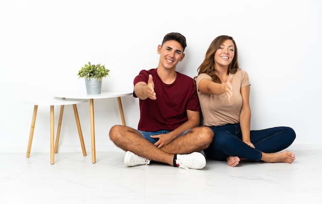 Photo young couple sitting on the floor on white shaking hands for closing a good deal