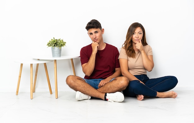 Young couple sitting on the floor on white thinking