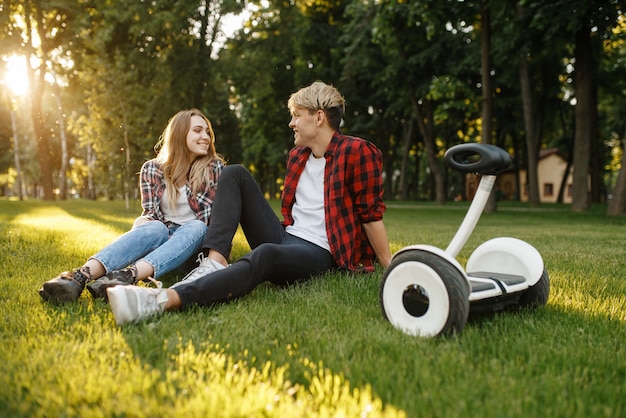 Young couple sitting on the grass near gyro board in summer park