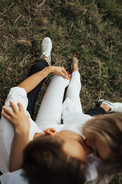 Young couple sitting on the green grass in a summer park, hugging and kissing. Selective focus, focus on hand.